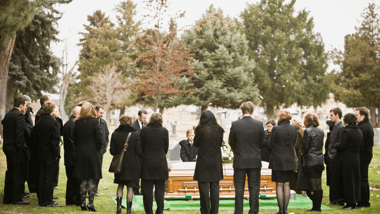 A group of people around a coffin in a graveyard.
