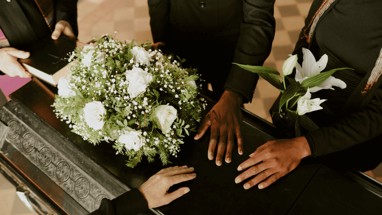 A group of people with their hands on a coffin and a priest looking on.