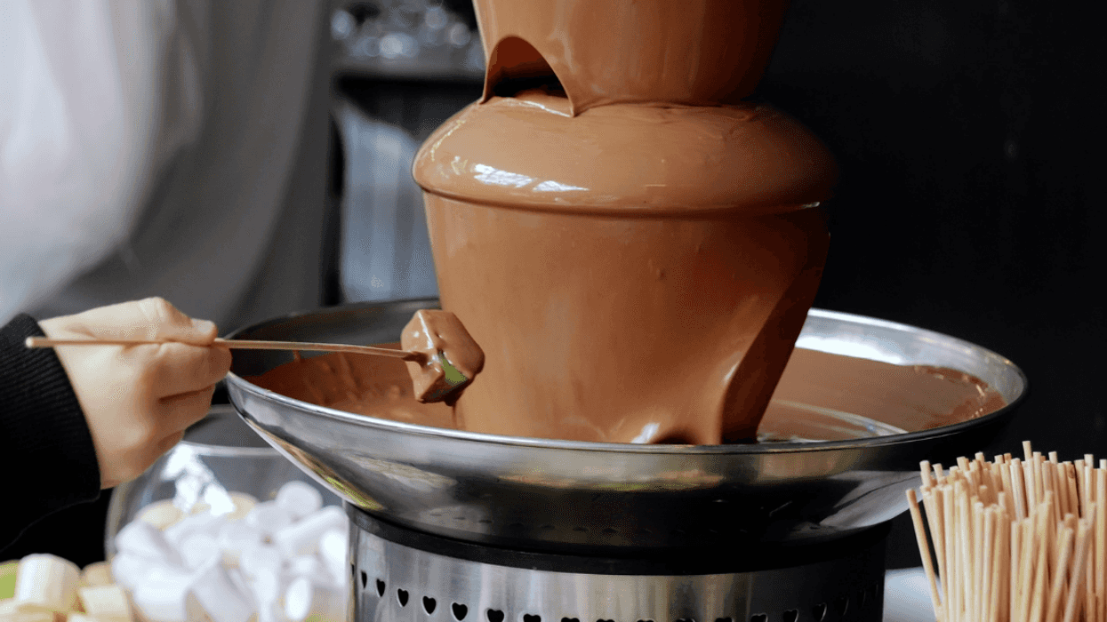 A hand dipping fruit in a chocolate fountain