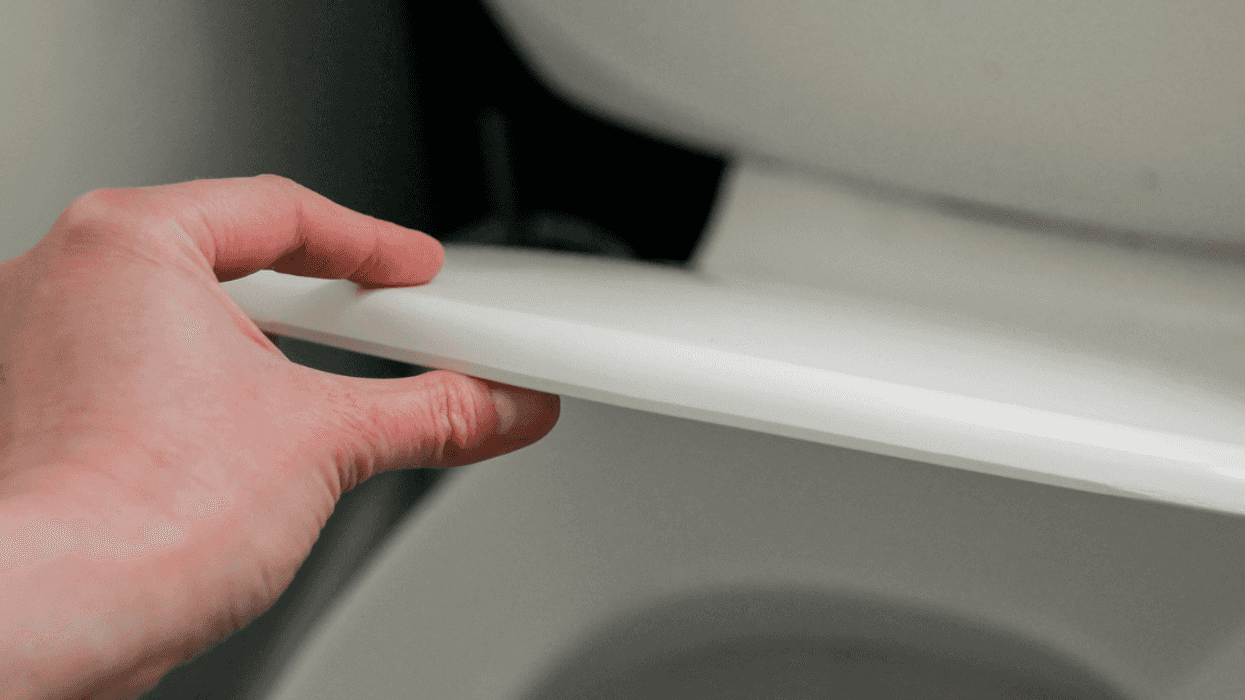 A hand picking up the lid of a toilet seat.