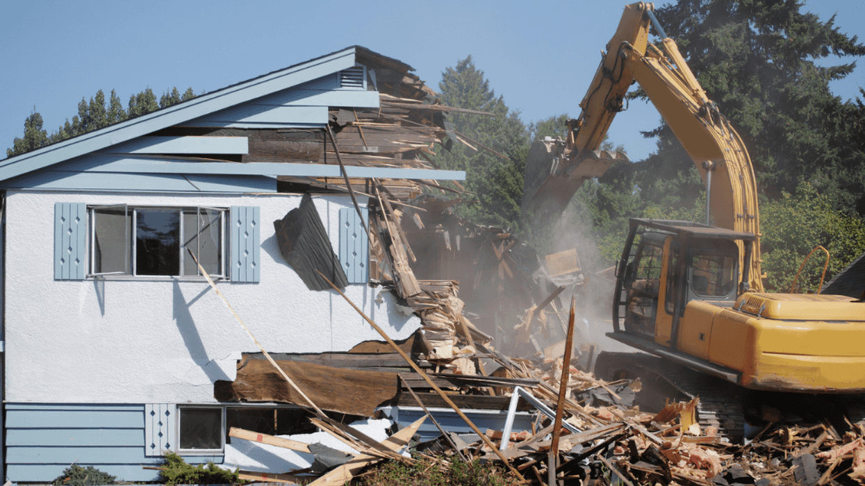 A house being torn down by a tractor.