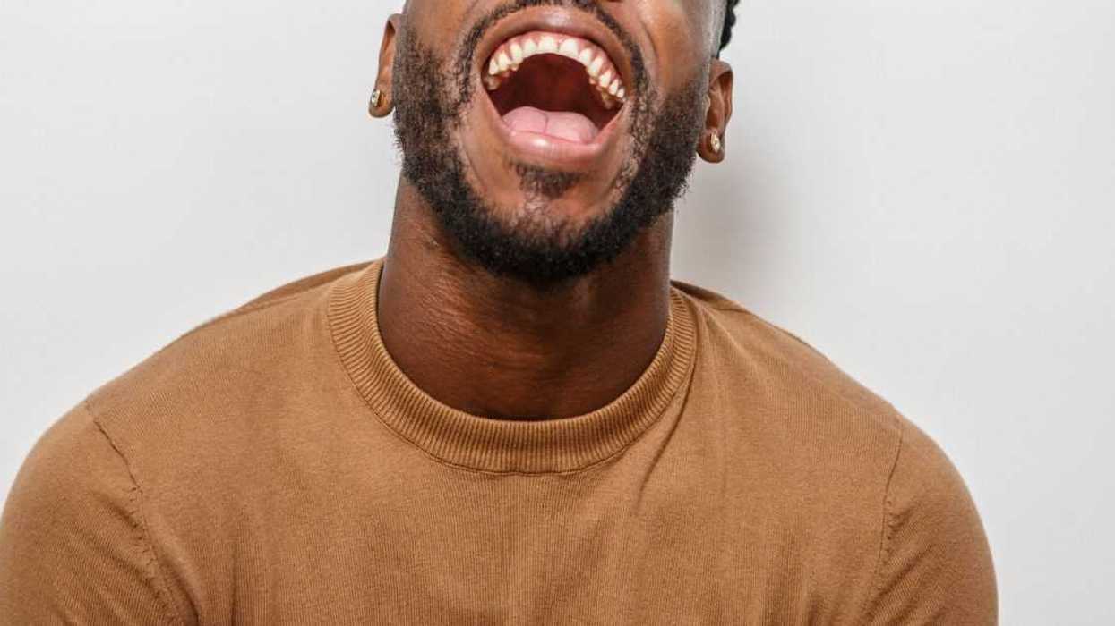 A joyful man is laughing with his head tilted back, showcasing a broad smile. He wears a cozy sweater, creating a cheerful atmosphere.