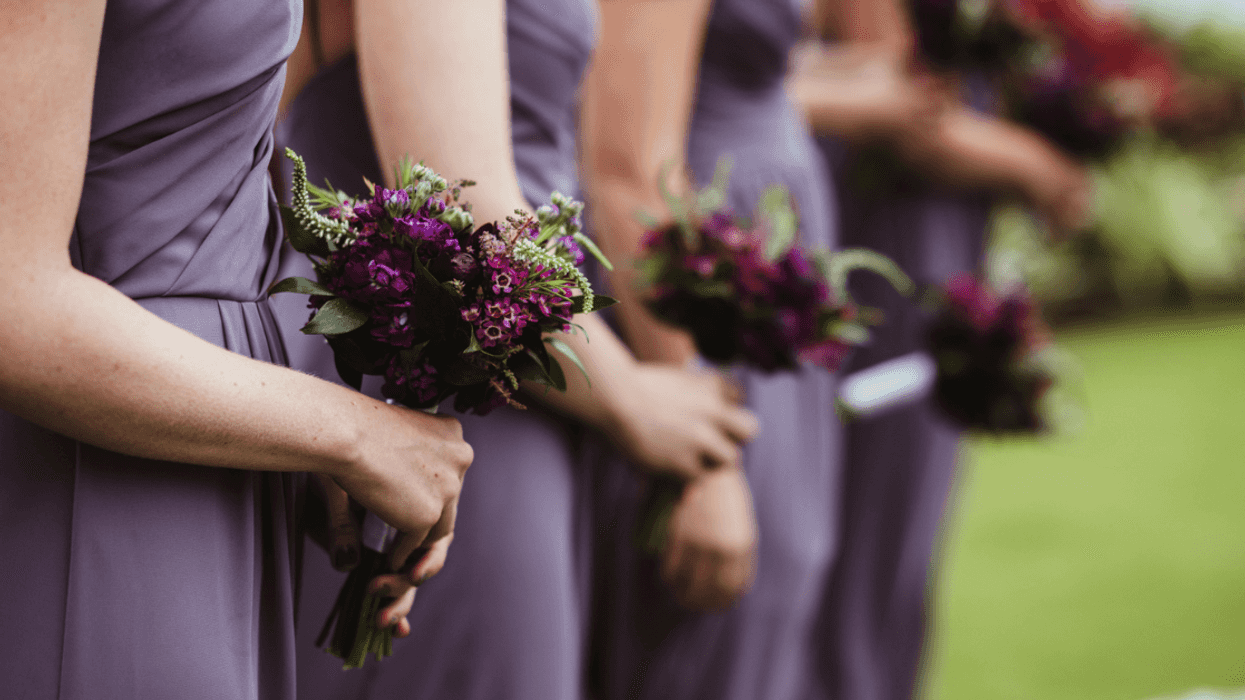 A line of bridesmaids in purple dresses holding bouquets.