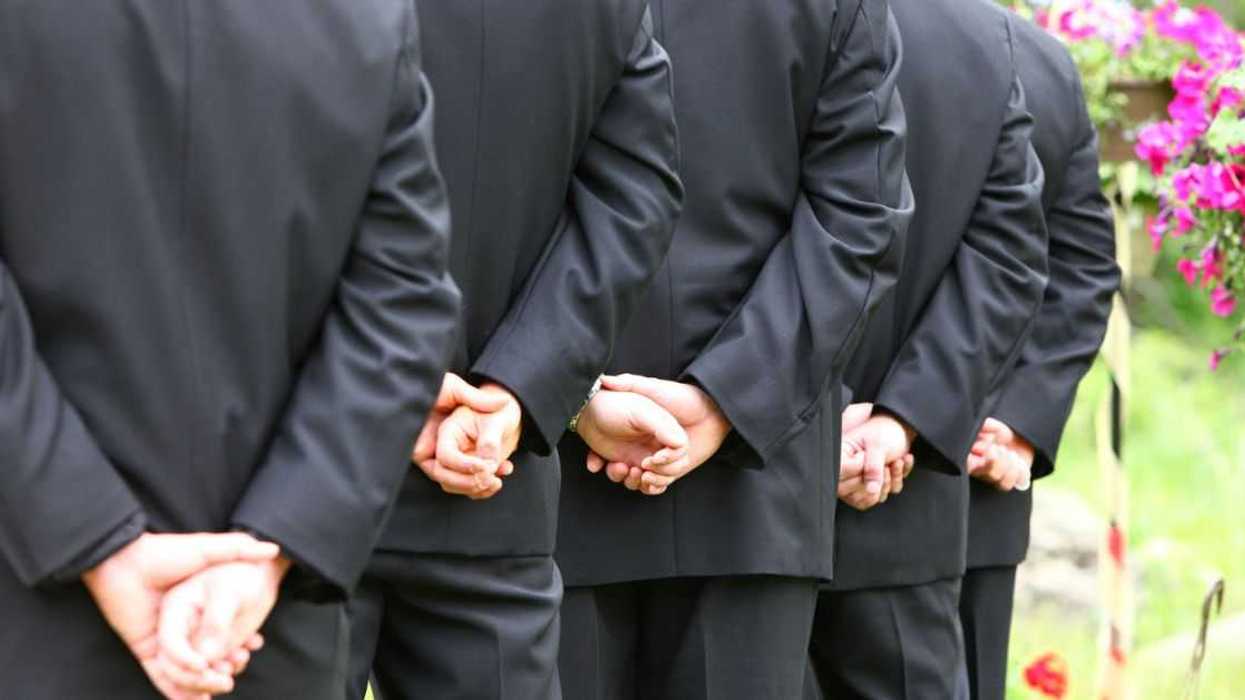 A lineup of groomsmen hands clasped during the wedding ceremony.