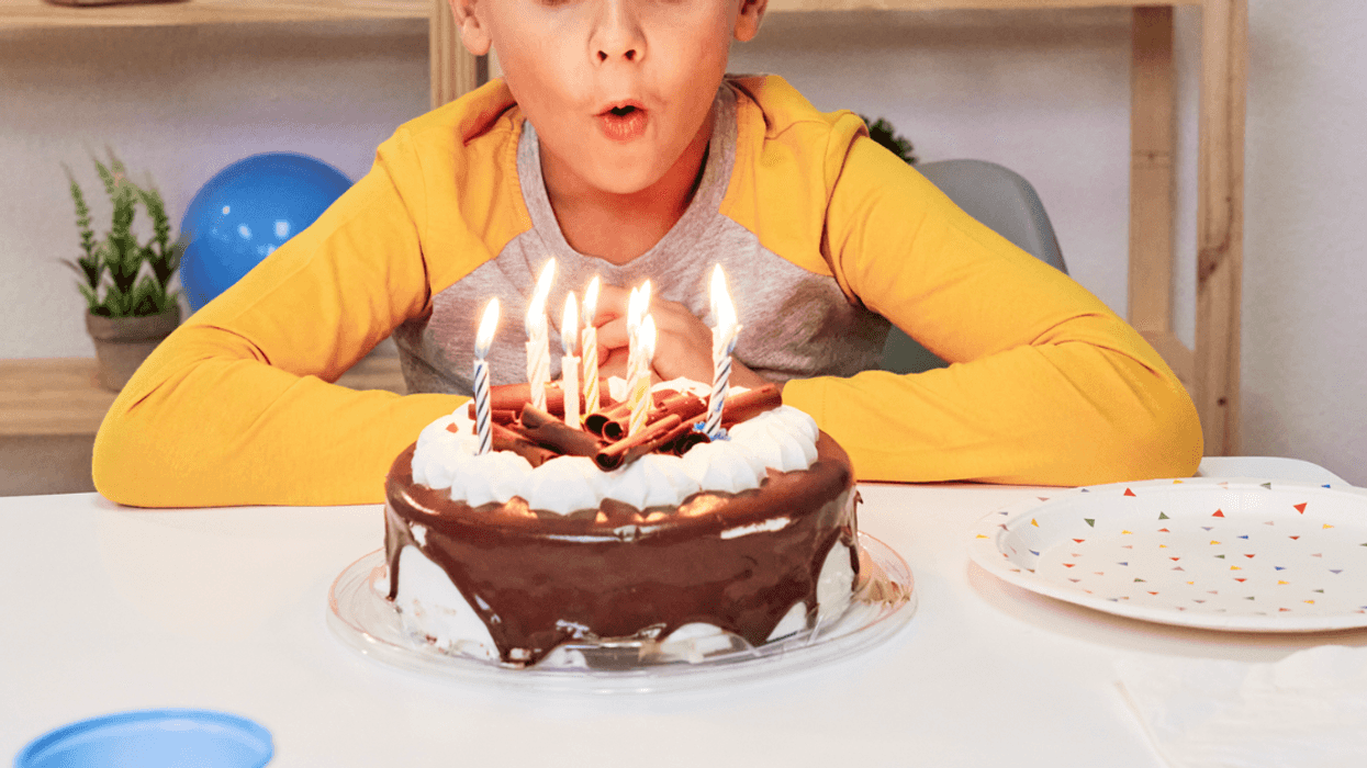 A little boy blowing out birthday candles on a chocolate cake.