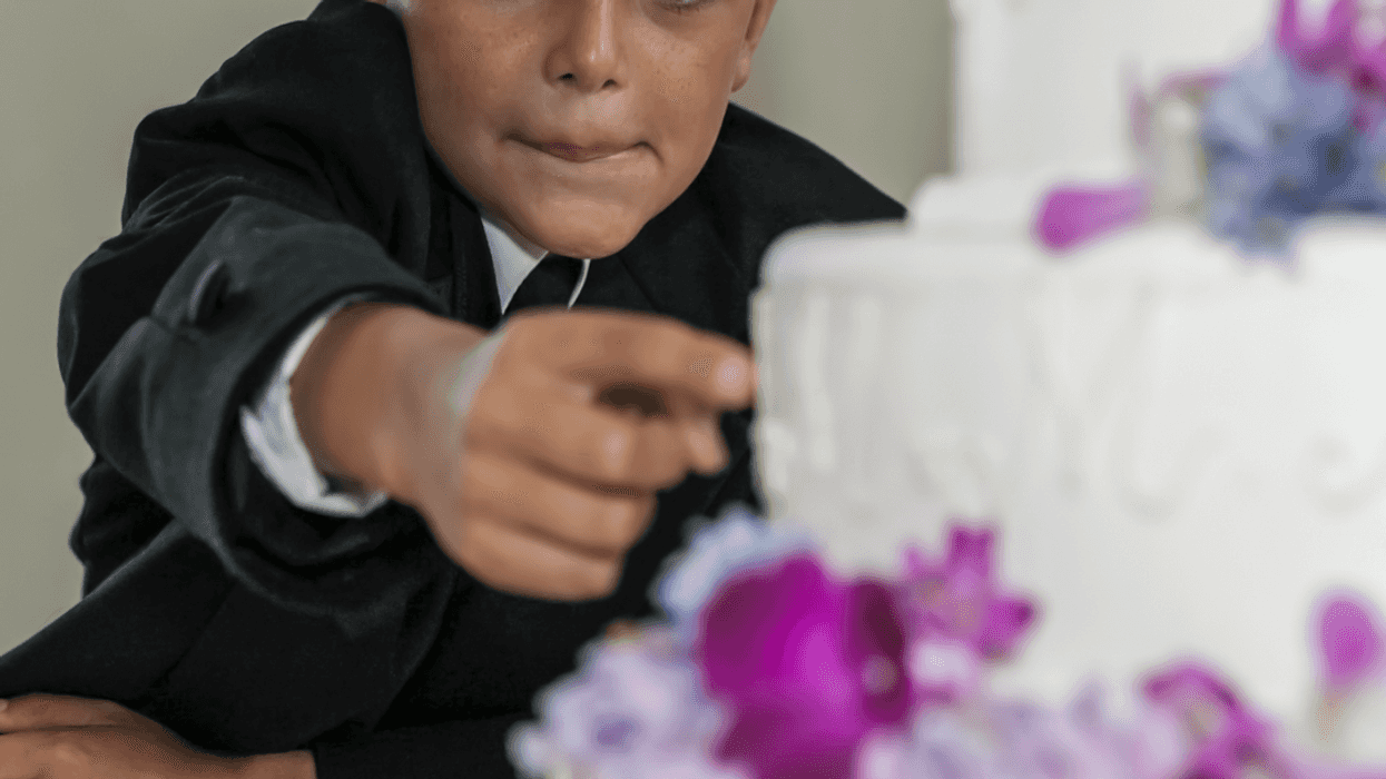 A little boy in a tuxedo reaching for a wedding cake.