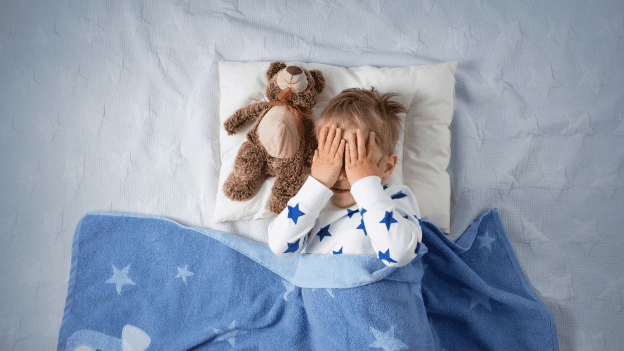 A Little boy in bed with his hands covering his eyes.