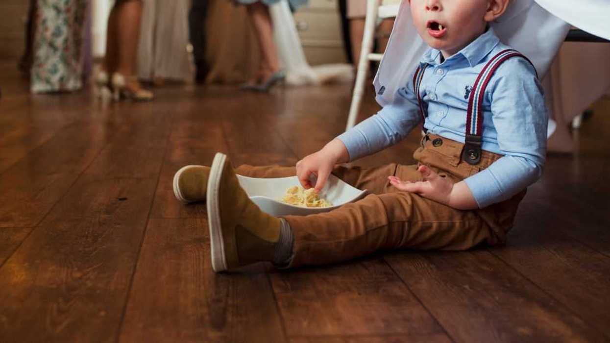 A little boy sits on the floor of a wedding eating food
