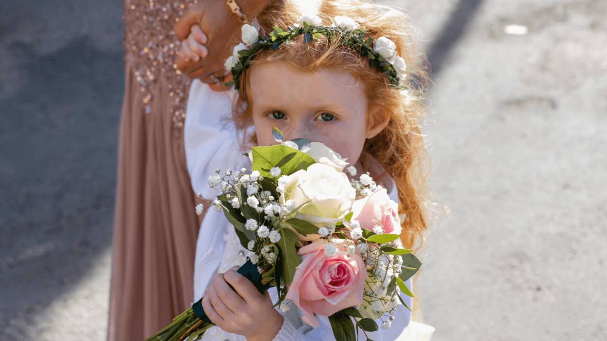 A little girl wearing a floral crown, and holding a bouquet in front of her face.