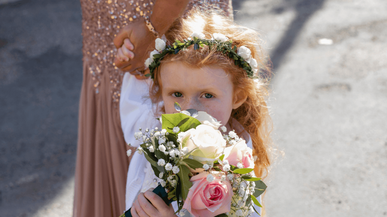 A little girl wearing a floral crown holding a bouquet in front of her face.