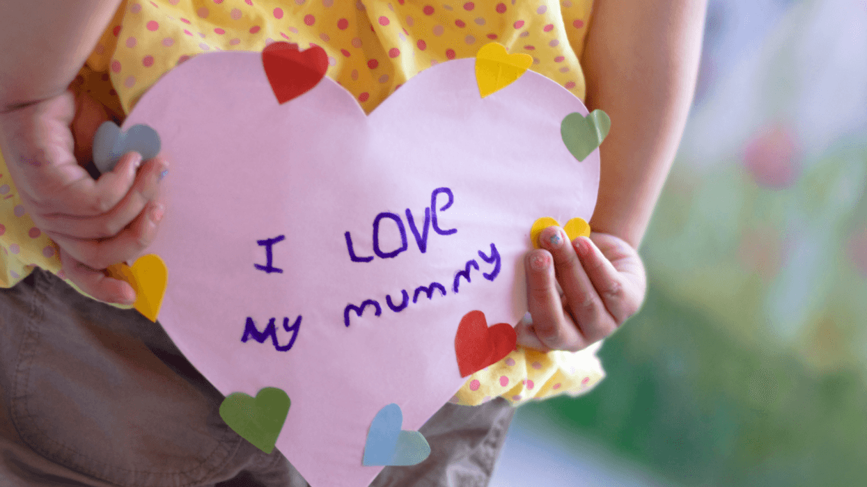 A littler girl holding a Mother's Day card behind her back.