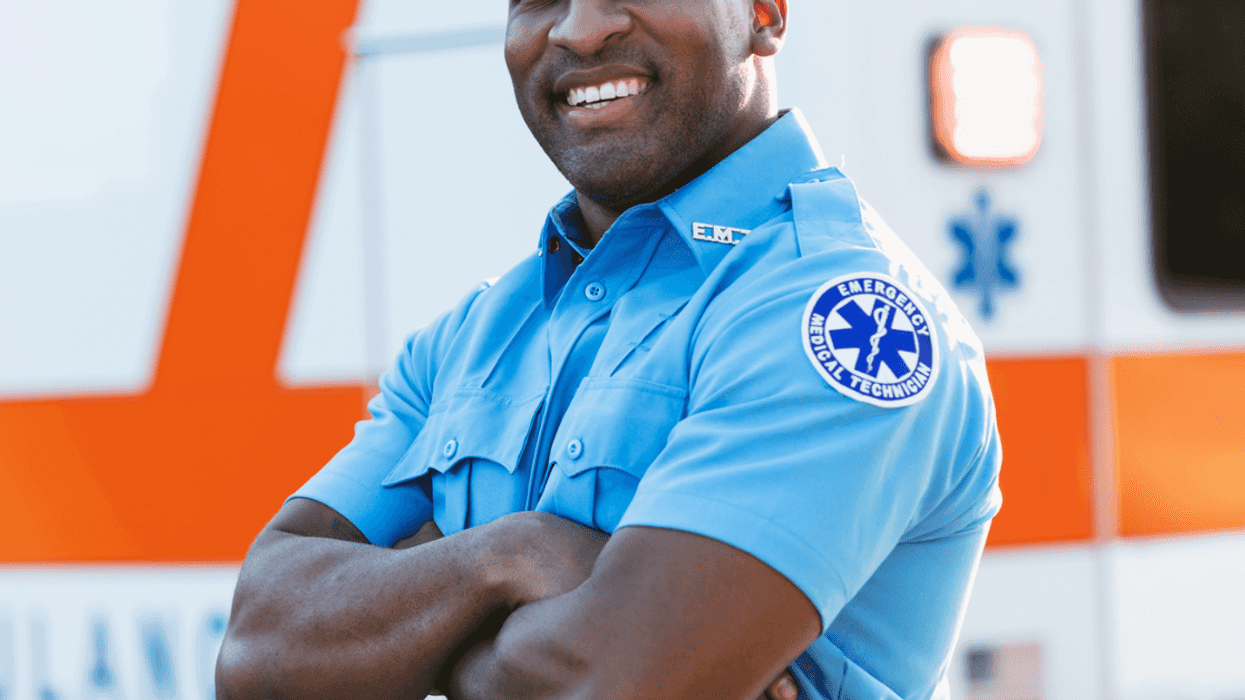 A male paramedic in uniform standing in front of an ambulance.