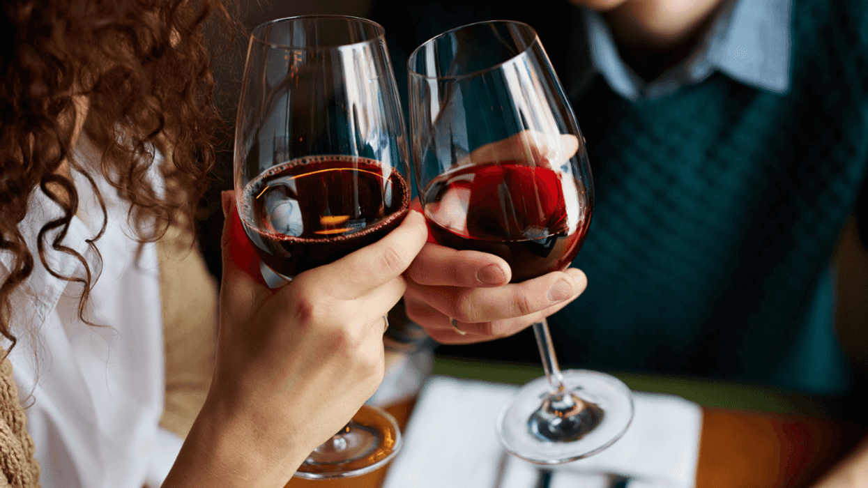 A man and a woman clinking glasses of red wine.