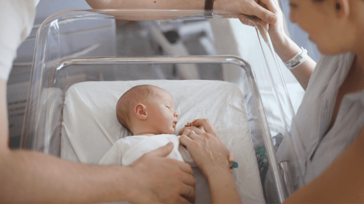 A man and a woman looking down at a baby in a hospital crib.