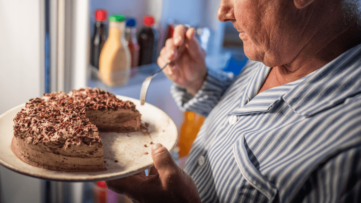 A man eating cake in front of the refrigerator.
