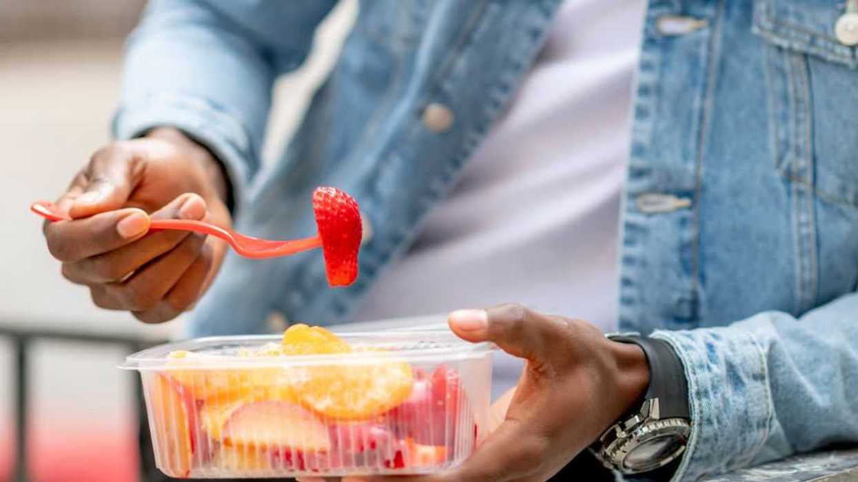 A man eats a strawberry from a container of fruit