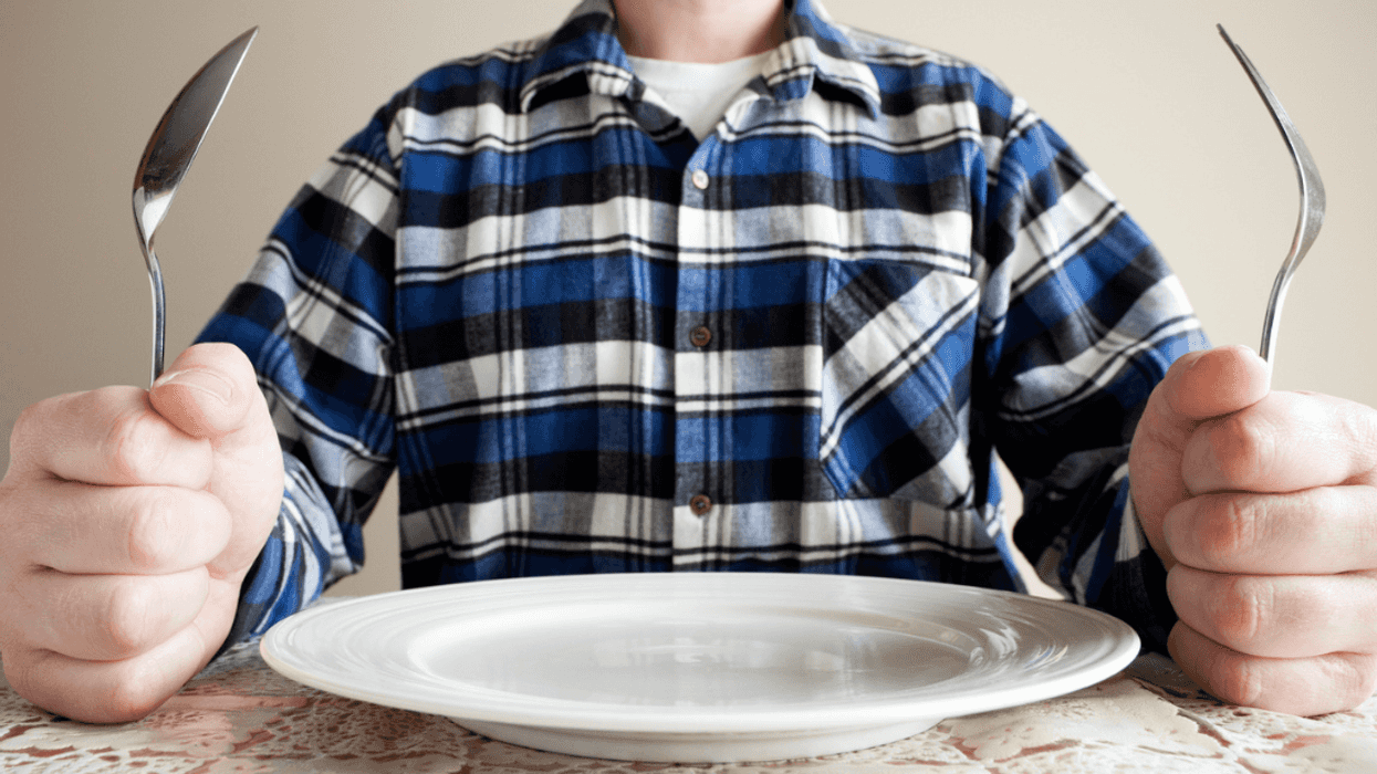 A man holding a fork and a spoon on each side of an empty plate.