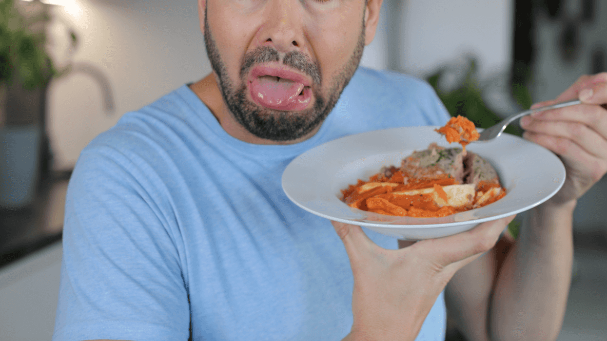 A man holding a plate of food with a grossed out expression on his face.