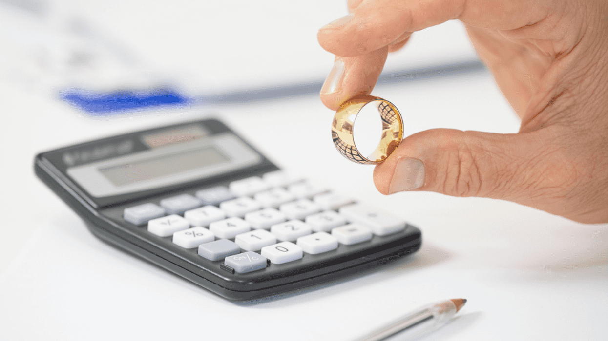 A man holding a wedding ring above a calculator