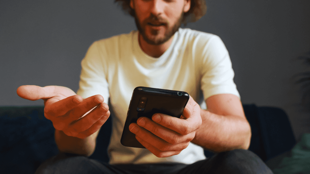 A man holding his phone in one hand and gesturing emphatically in another.