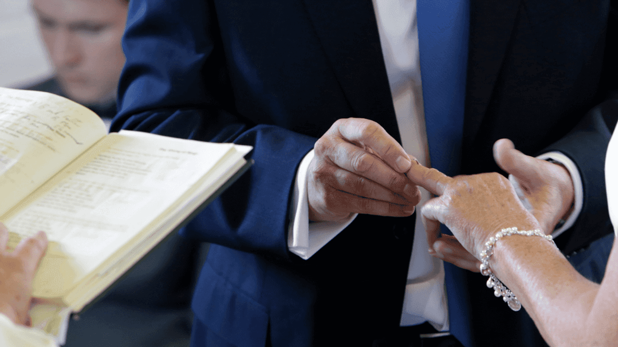 A man in a coat and tie placing a ring on a woman's finger.