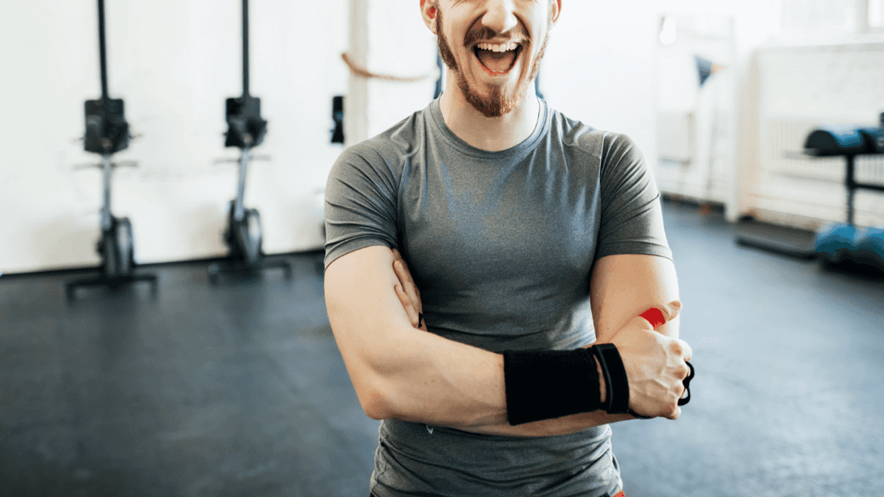 A man in a gym, folding his armns and laughing