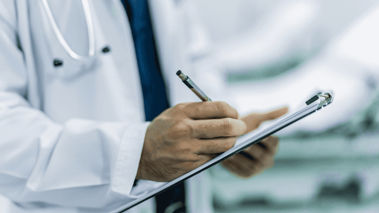 A man in a medical coat writing something on a clipboard