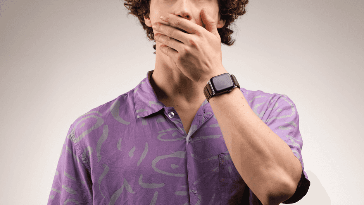 A man in a purple shirt with his hand over his mouth.