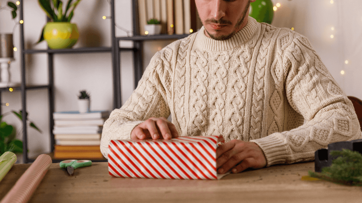 a man in a white sweater wrapping a christmas gift