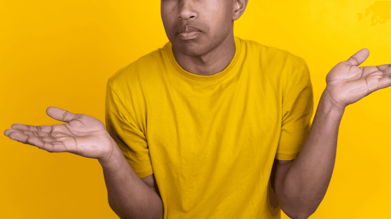 A man in a yellow shirt shrugging his arms.