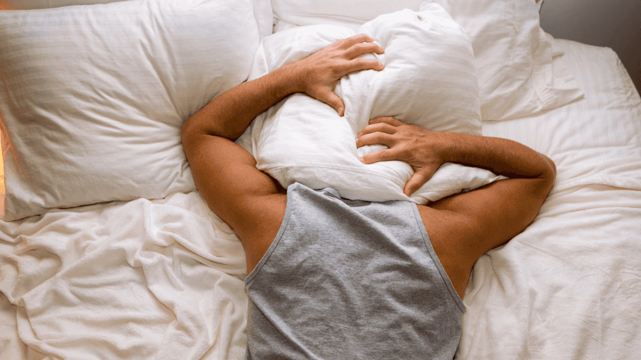 A man in bed with his head covered in pillows.
