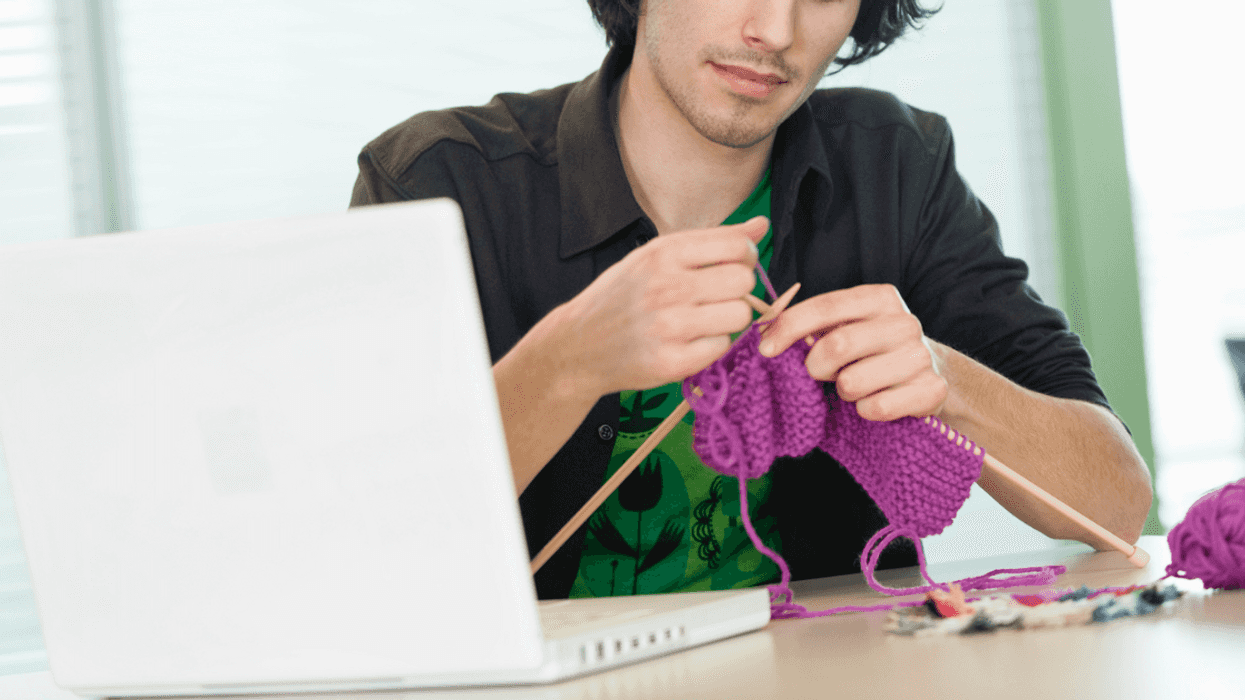 A man knitting at his office desk.