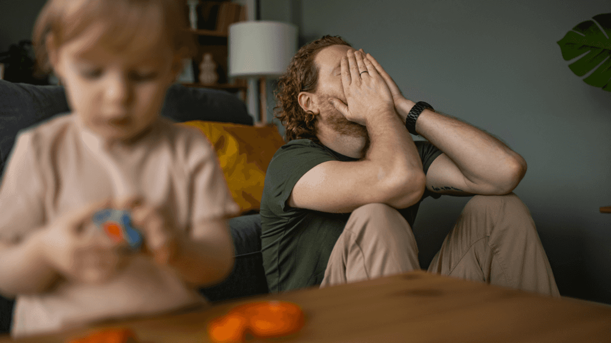 A man leaning against the sofa with his head in his hands and a child playing in front of him.