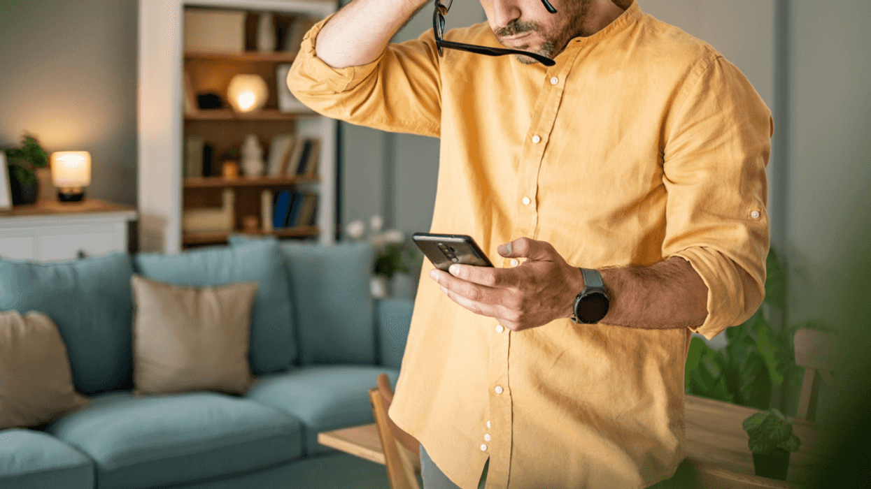 A man looking down at his cell phone holding his head in his hands.