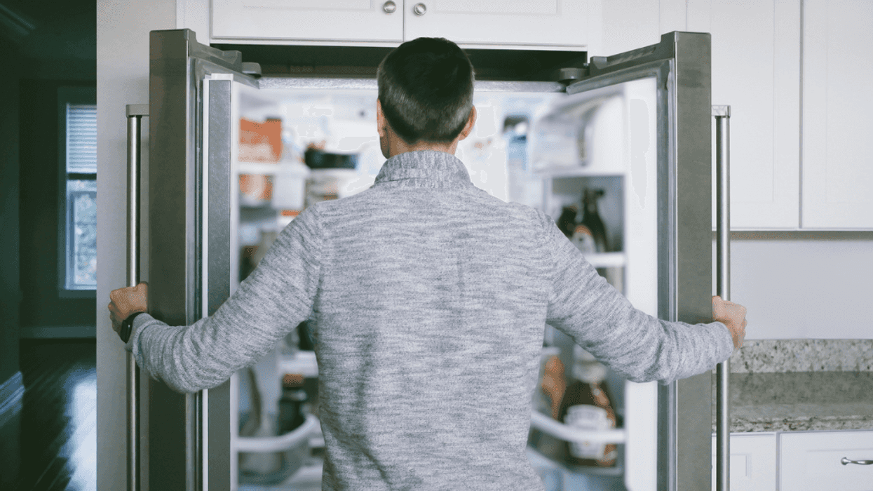 A man looking into an open refrigerator.