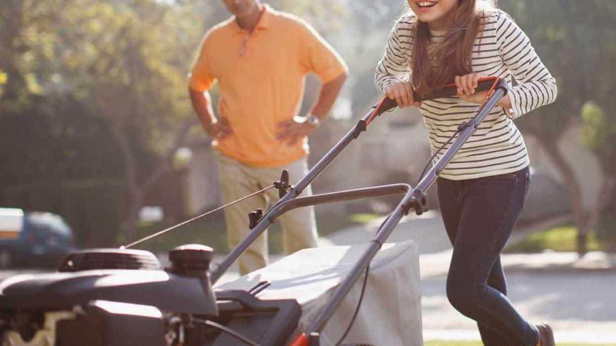 A man looks on as a young girl mows the lawn