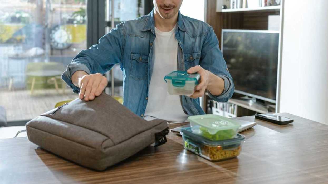 A man organizes lunch boxes while preparing for his day. The background shows a modern living space. This action emphasizes preparation, organization, and a healthy lifestyle.