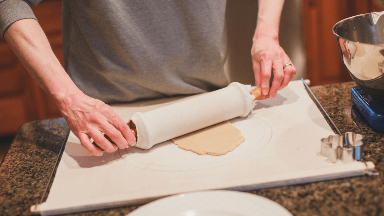 A man rolling a piece of dough on a rolling board with a rolling pin.