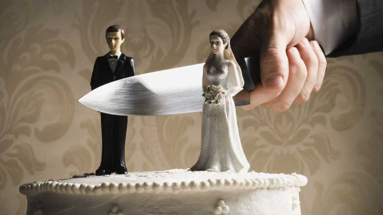 A man's hand holds a large knife between bride and groom cake toppers.