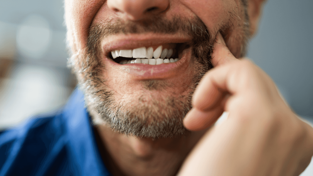 A man showing his teeth and massaging his jaw.