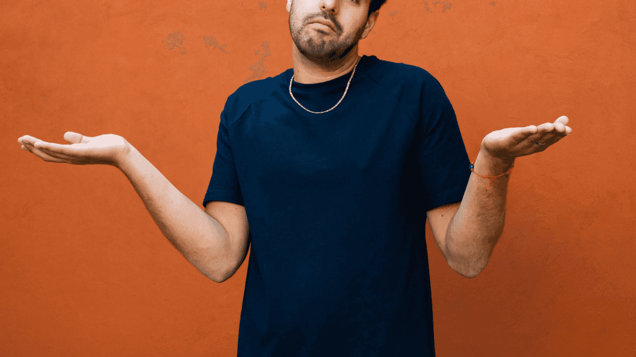 A man shrugging his shoulders in front of an orange wall.