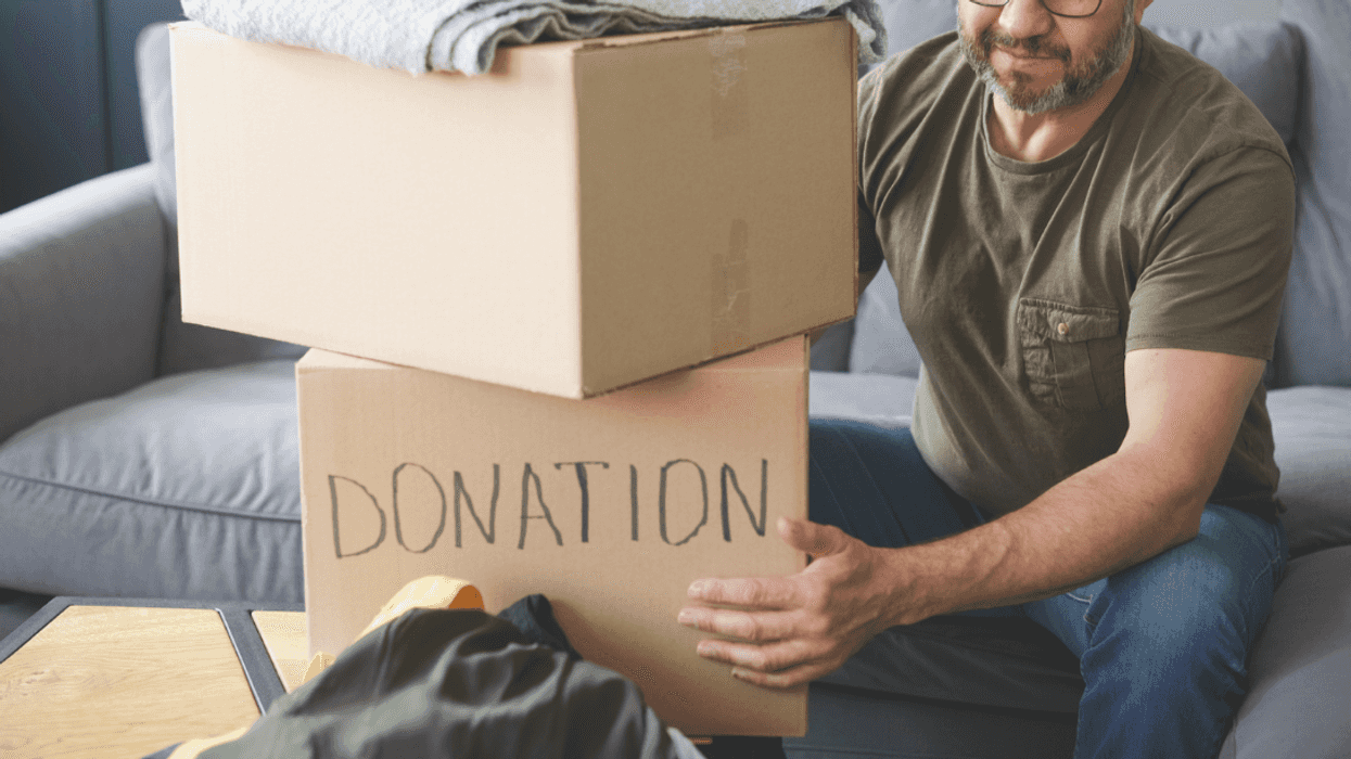 A man sitting behind two stacked cardboard boxes, with one having "donations" written on it.