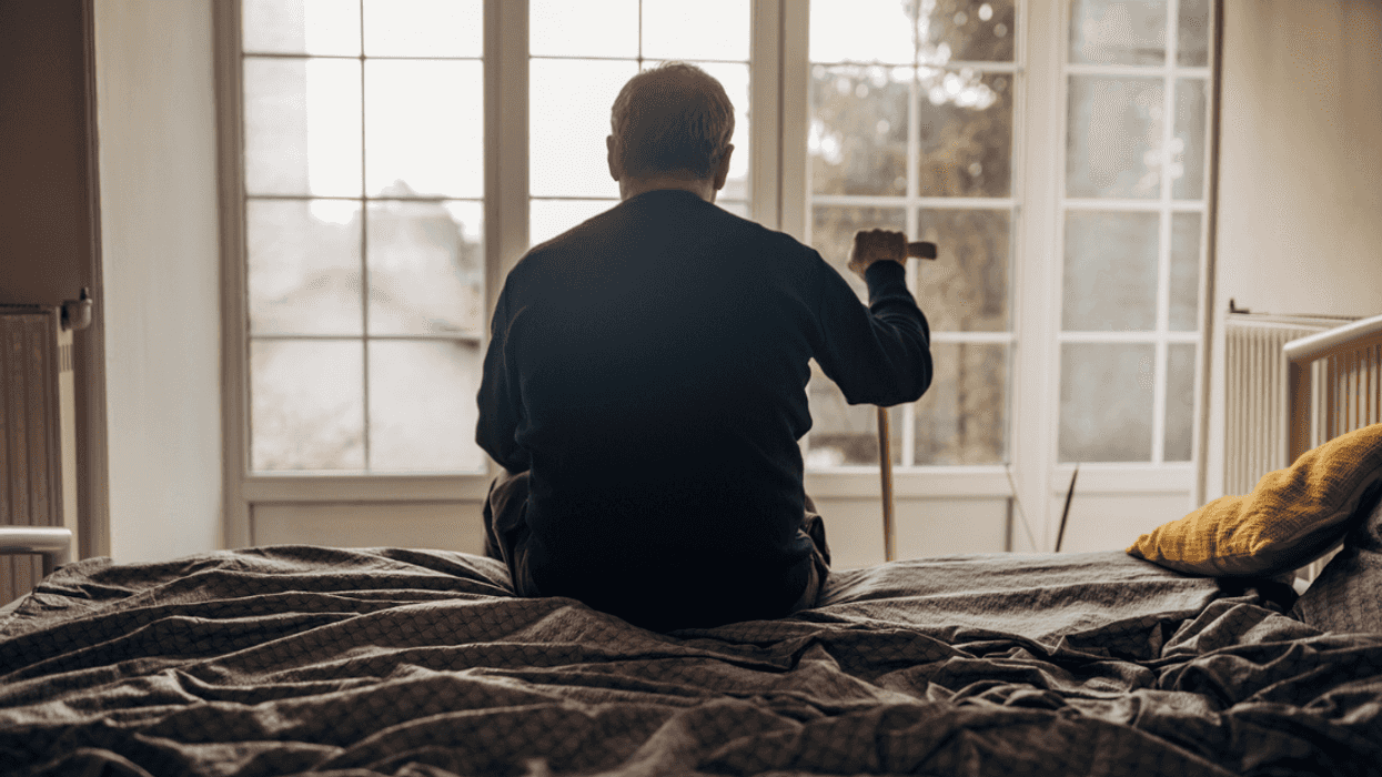 A man sitting on the edge of a bed holding a cain.