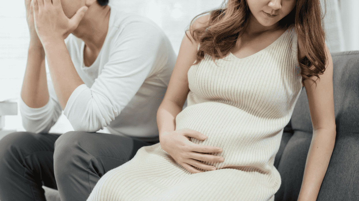 A man sitting on the sofa with his head in his hands sitting next to a pregnant woman.