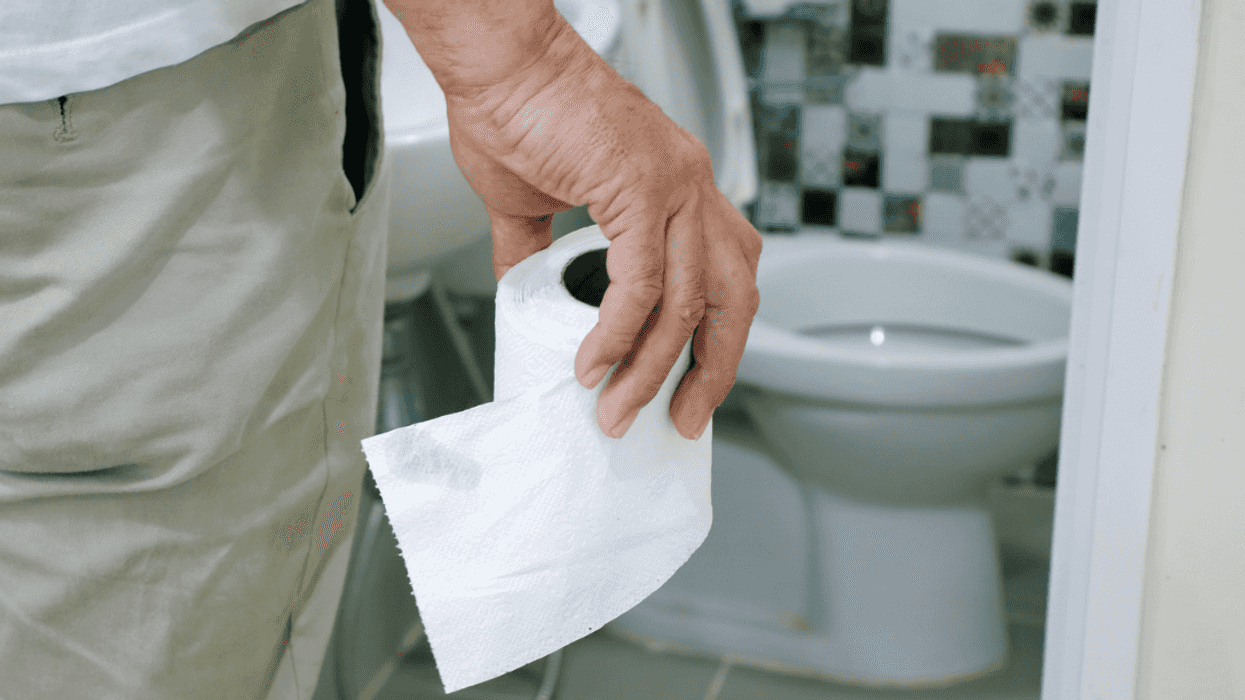 A man standing in front of a toilet holding a roll of paper towels.