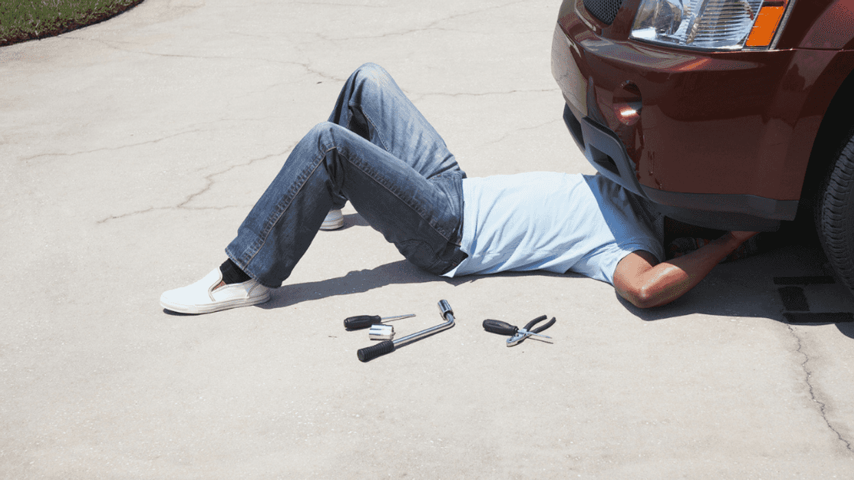 A man under the front of a car with tools laying by his side.