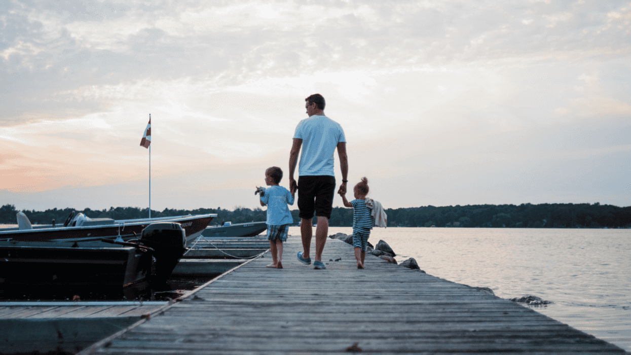A man walking down the dock holding the hands of two children.