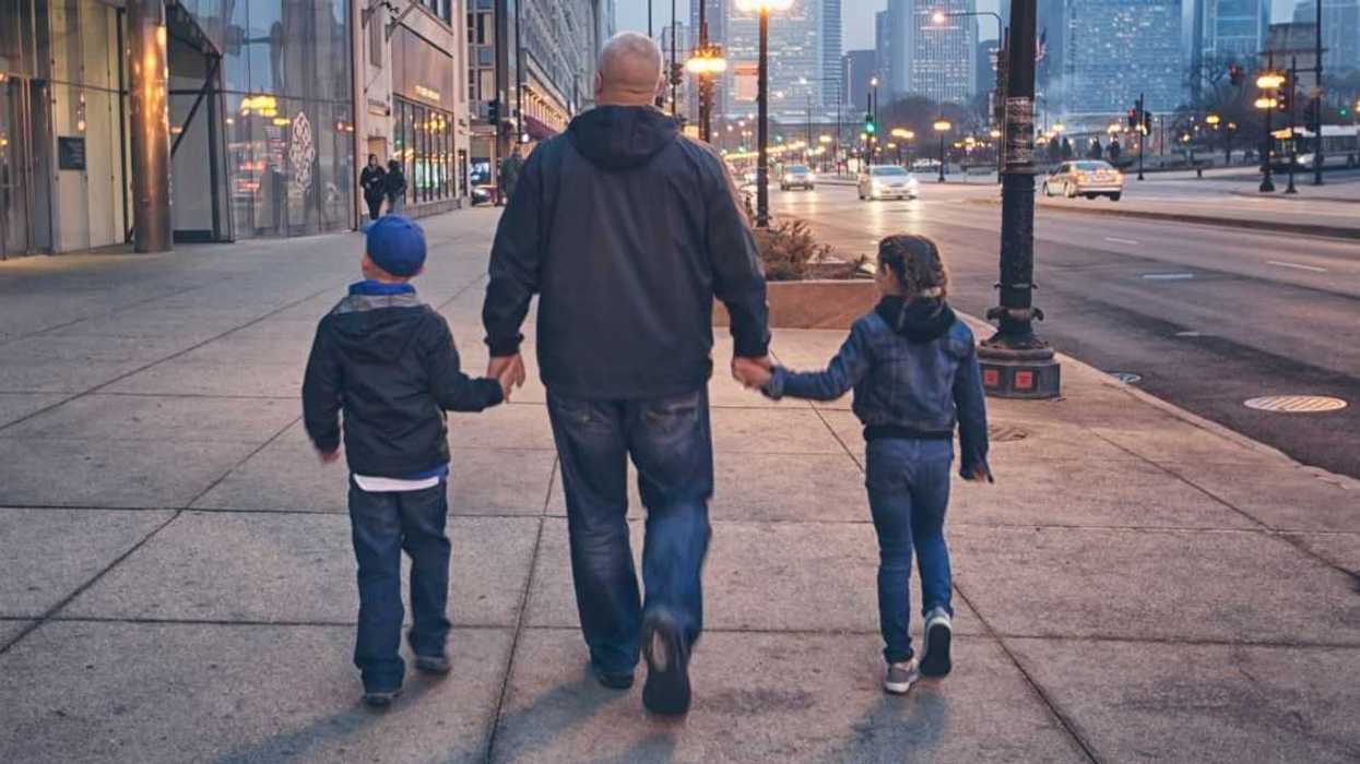 A man walks down the street holding the hands of two children