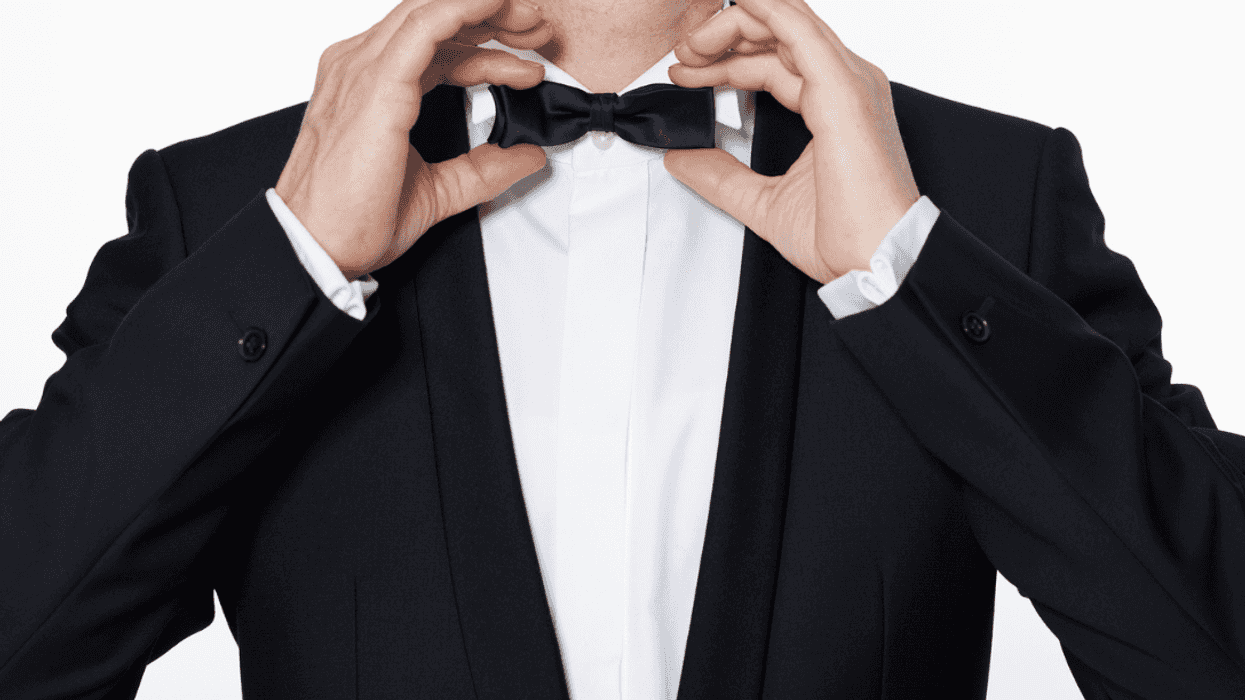 A man wearing a tuxedo fixing his bow tie,