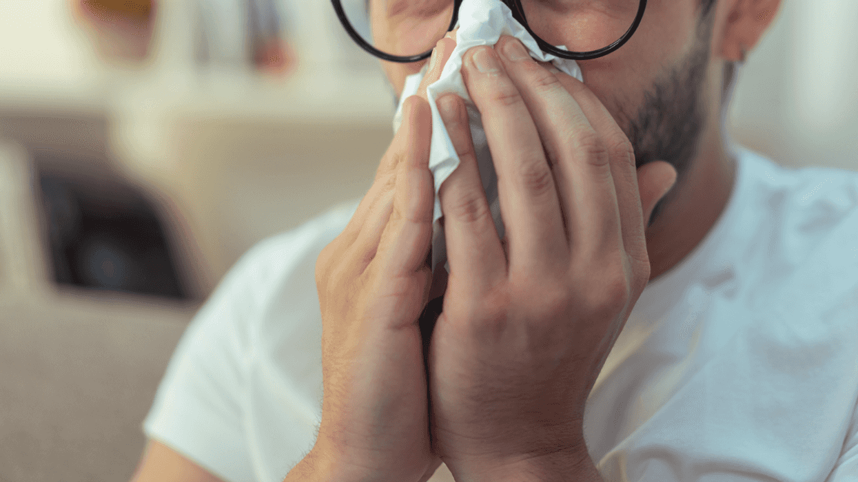 A man wearing large glasses holding a tissue to his nose.